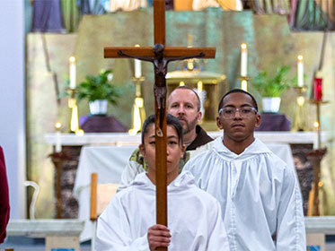An alter server holding up a crucifix as they exit Mass